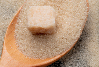 top view of a wooden spoon with granulated brown sugar and sugar cube on black background